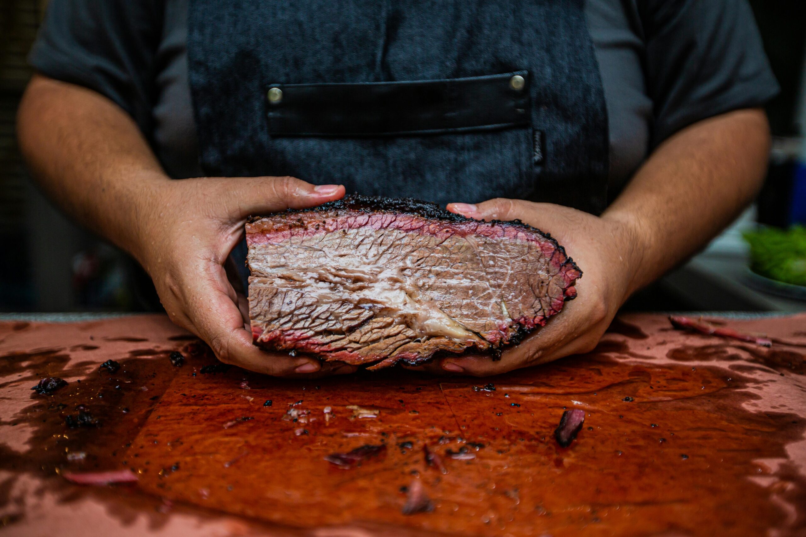 Close-up of hands holding a juicy smoked beef brisket on a wooden cutting board, showcasing rich texture.